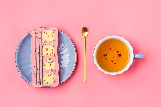 rosa Schokolade mit Rosinen und Nüssen auf Fliederplatte, Tasse schwarzen Tee, goldener Löffel auf rosa