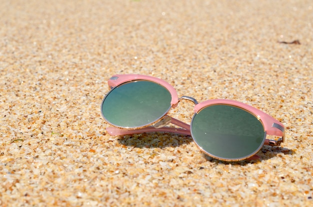 Rosa Sonnenbrille gegen die Sonne auf dem Strandsand