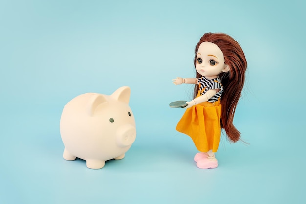 rosa Sparsamkeit und Puppe auf blauem Hintergrund Konzept der Erhöhung des Einkommens aus Bankkonten Ersparnisse kleines Kind Puppe mit einer Münze in den Händen auf blauen Hintergrund