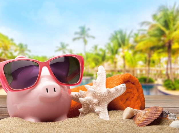 Rosa Sparschwein mit Sonnenbrille über Meer-Swimmingpool-Hintergrund. Einsparungen für Urlaubskonzept