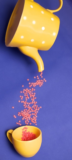 Rosa Sterne fallen aus einer gelben Teekanne in einer Tasse auf einen lila Hintergrund