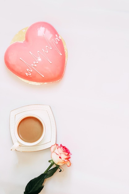 Rosa Teerose mit herzförmigem rosa Mousse-Kuchen mit einer Tasse Kaffee