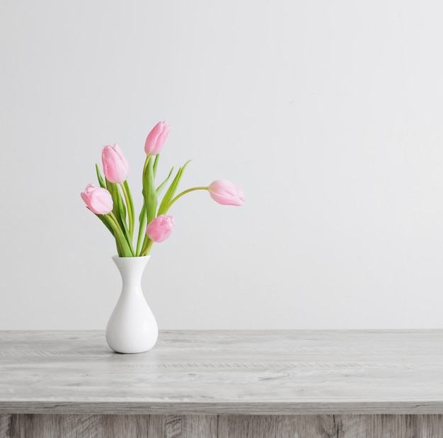 Rosa Tulpen in der weißen Keramikvase auf Holztisch auf weißer Hintergrundwand
