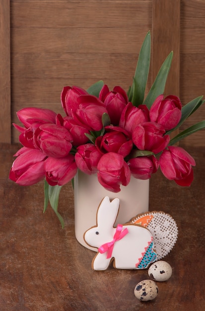 Rosa tulpen und osterhasenplätzchen auf holzoberfläche. frühlings- oder osterkonzept