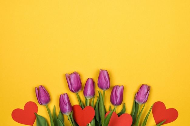 rosa Tulpen und rote Herzen auf gelber Wand