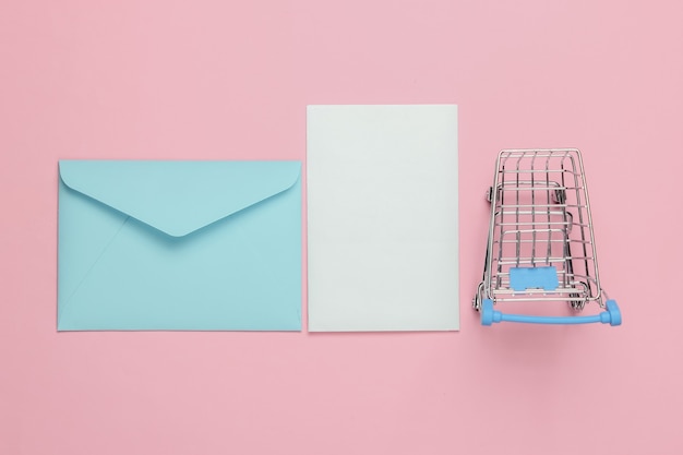 Rosa Umschlag mit Brief und Einkaufswagen auf rosa Pastellhintergrund. Modell für Valentinstag, Hochzeit oder Geburtstag. Draufsicht
