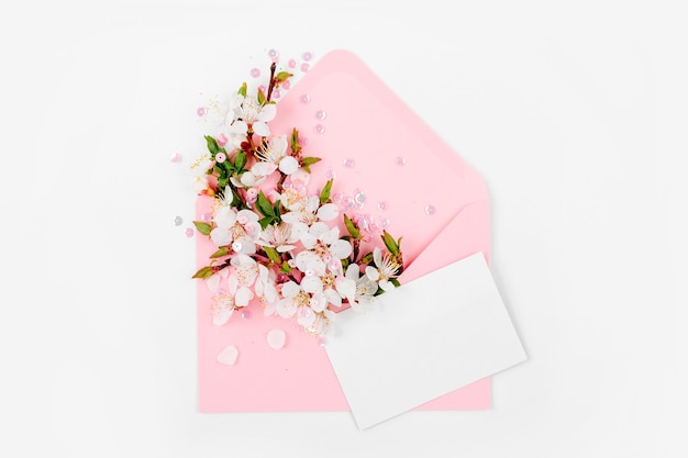 Rosa Umschlag mit leerer Karte und einem Frühlingsblumenarrangement. Flache Lage, Ansicht von oben.
