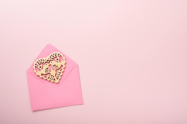 Rosa Umschlag mit weißem durchbrochenem Herzen und rotem Band auf rosa Hintergrund. Draufsicht mit Kopienraum. Valentinstag oder Hochzeit romantisches Konzept. Festliche Komposition. Attrappe, Lehrmodell, Simulation.