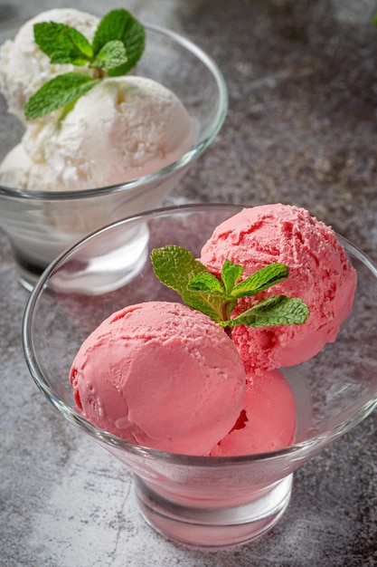 Rosa und cremige Erdbeer-Minz-Creme-Eiskugeln im Becherglas auf grauem Stein