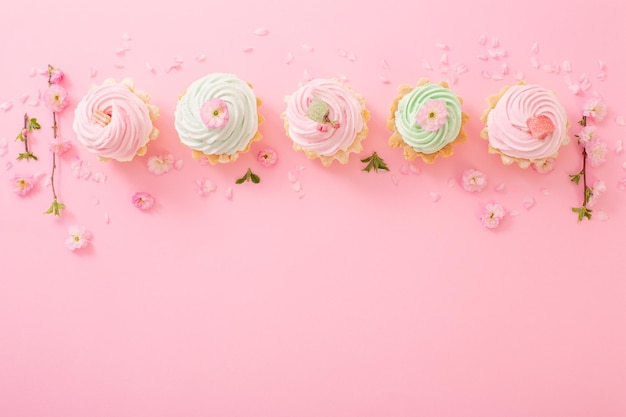 Rosa und grüne kleine Kuchen mit Frühlingsblumen auf rosa Hintergrund