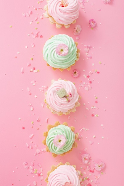 Rosa und grüne kleine Kuchen mit Frühlingsblumen auf rosa Hintergrund