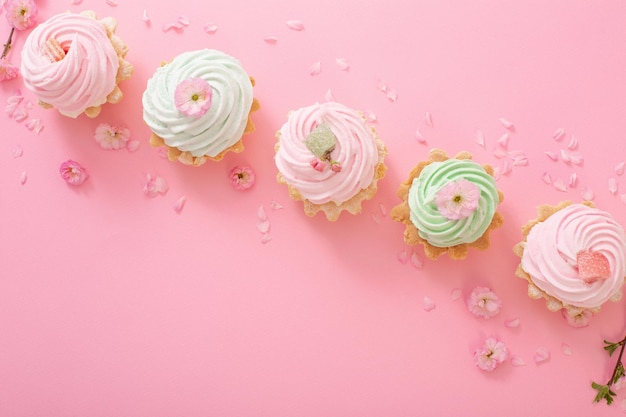 Rosa und grüne kleine Kuchen mit Frühlingsblumen auf rosa Hintergrund