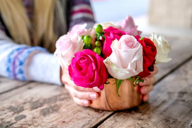 Rosa und weiße Rosen im kupfernen Teller in den Händen der Frau auf strukturiertem Holztisch Café im im Freien. Lifestyle-Konzept.