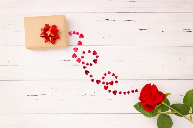 Rosa vermelha, caixa de presente e corações em fundo de madeira