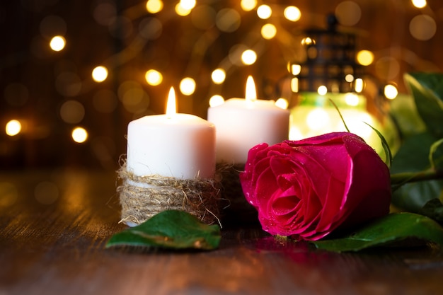 Rosa vermelha e lanterna com luzes sobre uma mesa de madeira.