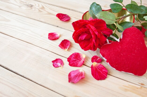 Rosa vermelha fresca com pétalas e coração em fundo de madeira