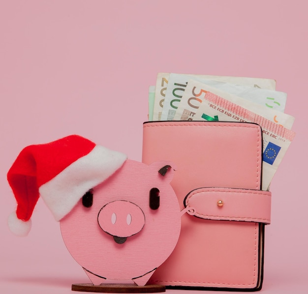 Rosa Weihnachtsschwein und Geldbörse mit Euro auf rosa Hintergrund