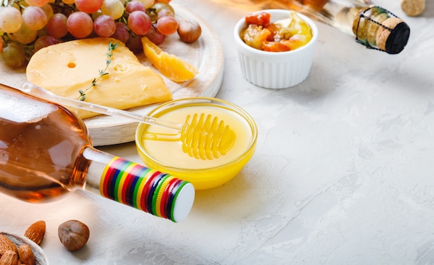 Rosa Weinkomposition auf hellgrauem rustikalem Betonhintergrund mit Kopienraum. Roséweinflaschen-Käse-Nüsse und rosa Trauben, Honig. Camembert-Käse, Snacks in der Weinbar.