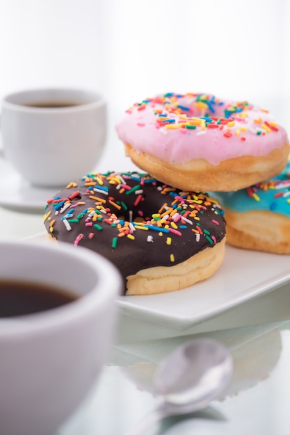 Rosado, azul y chocolate rocían donas en un plato blanco y una taza de café