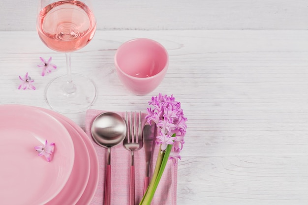 Rosafarbene rustikale Tischdekoration mit lila Hyazinthenblumen-Leinenserviette und Glas Roséwein auf weißem Holztisch