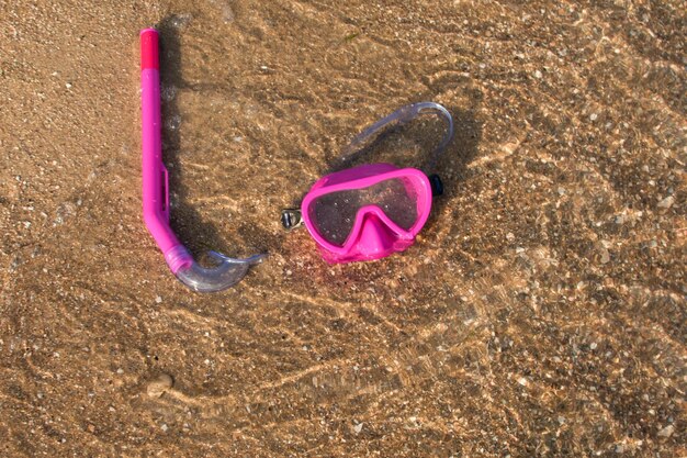 Rosafarbene Schwimmmaske und Tauchschnorchel liegen im Sand am Wasser