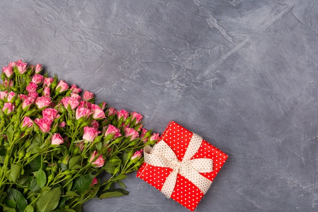 Rosas de aerosol rosa, regalo en caja roja sobre fondo gris. Concepto del día de la mujer Día de San Valentín de la madre Copia espacio