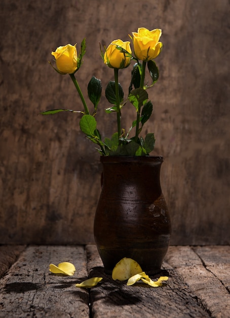 Rosas amarelas em um vaso em um fundo de madeira