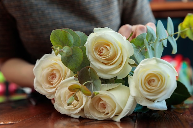 Las rosas blancas se encuentran en una mesa de madera. Las manos de la floristería están haciendo un ramo.