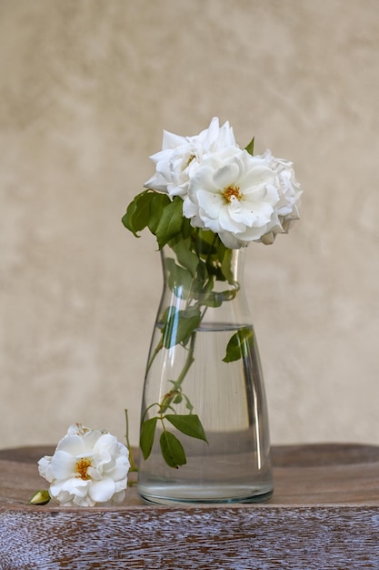 Rosas blancas en un jarrón de cristal sobre una tabla de madera texturizada y un fondo claro