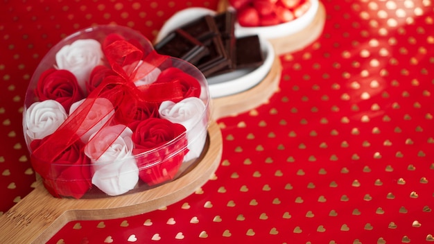 Foto rosas, bombones y dulces en platos en forma de corazón. ajuste de la tabla festiva para la fecha de los enamorados. fondo rojo