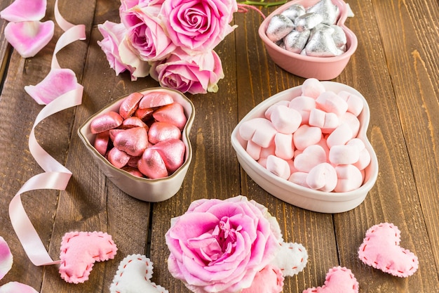 Rosas cor de rosa com chocolates na mesa de madeira rústica.