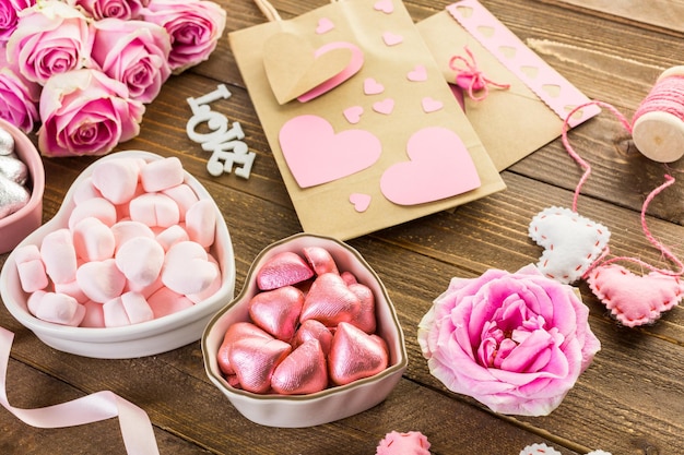 Rosas cor de rosa com chocolates na mesa de madeira rústica.