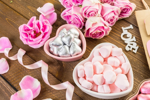 Rosas cor de rosa com chocolates na mesa de madeira rústica.