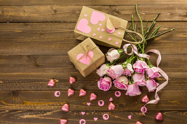 Rosas cor de rosa e presente embrulhado em papel reciclado na mesa de madeira rústica.