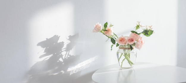 rosas cor de rosa em frasco de vidro na mesa branca moderna na parede branca de fundo
