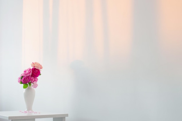 Rosas cor de rosa em vaso branco na mesa na parede branca de fundo