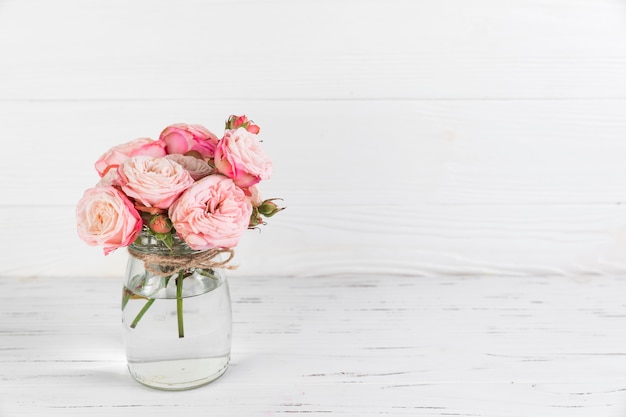 Rosas cor de rosa flor na jarra de vidro no pano de fundo texturizado de madeira branca