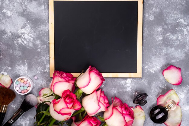 Rosas y cosméticos decorativos con una pizarra.