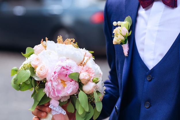 Rosas e peônias em um elegante buquê de casamento segurado pelo noivo