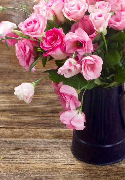 Rosas frescas e flores eustoma em vaso azul fecham na mesa de madeira