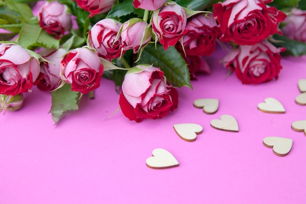 Rosas rojas con corazones de madera sobre un fondo rosa