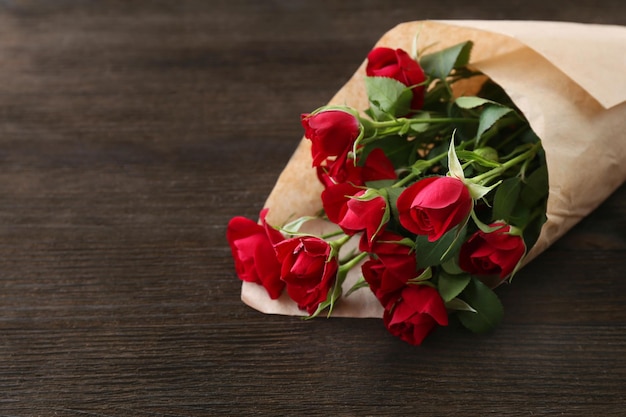 Rosas rojas envueltas en papel sobre fondo de mesa de madera