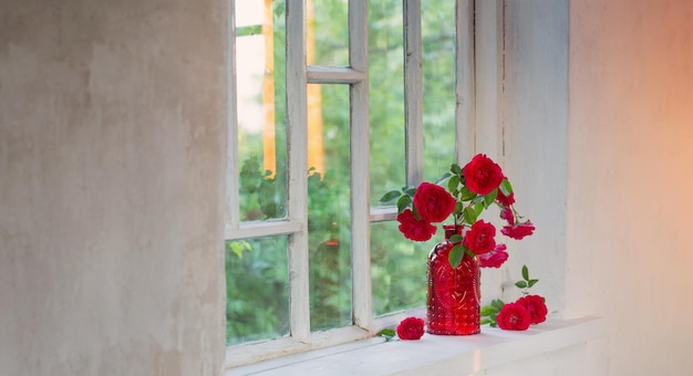 rosas rojas en un jarrón de vidrio rojo en el alféizar de la ventana