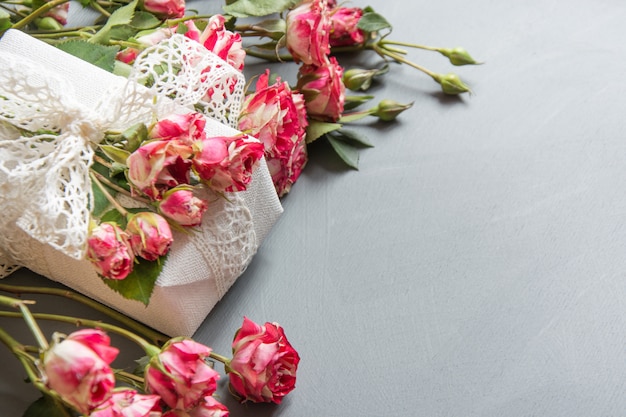 Rosas rosadas del arbusto y regalo femenino en gris