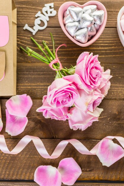 Rosas rosadas con chocolates sobre mesa de madera rústica.