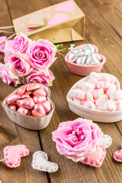 Rosas rosadas con chocolates sobre mesa de madera rústica.