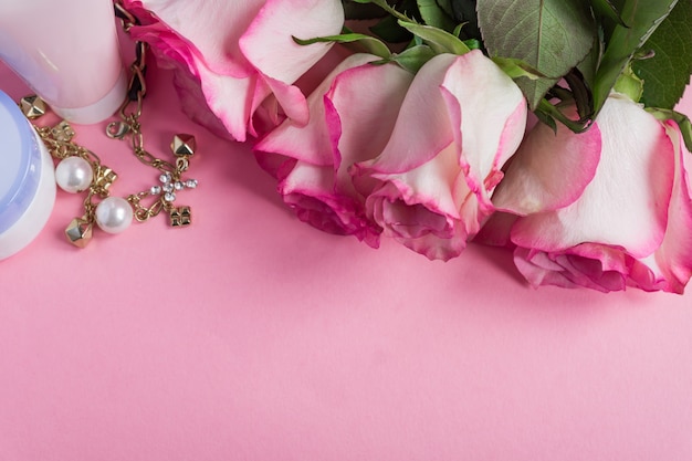 Rosas rosadas y crema para la cara sobre fondo de color rosa pastel. Marco floral romántico cuidado de la piel. Copia espacio