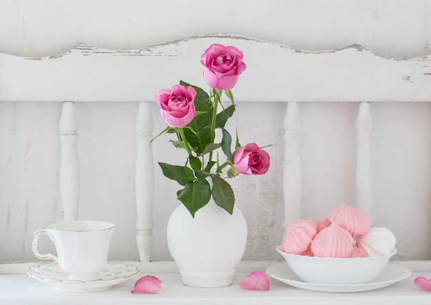 Rosas rosadas en florero y vajilla en estante de madera blanca