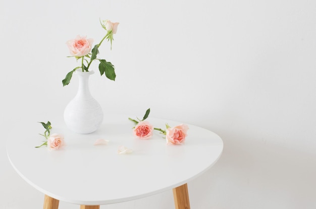 Rosas rosadas en jarrón blanco sobre la mesa en la pared blanca de fondo