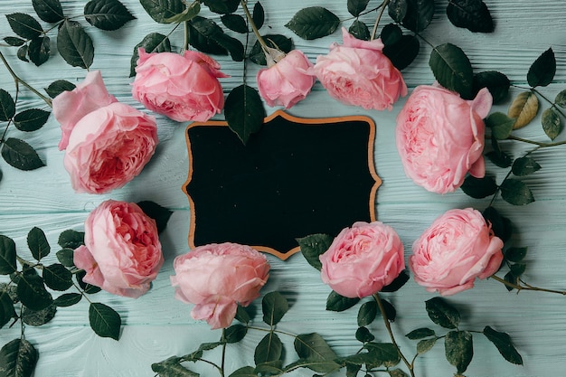 Rosas rosas y un marco de fotos en una mesa azul.